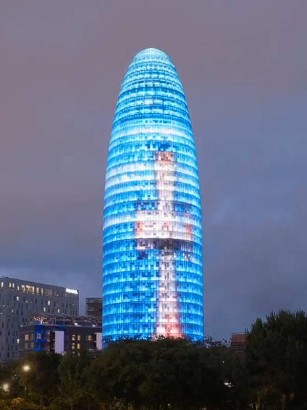 Torre Glòries iluminada en Barcelona para dar la bienvenida al Papa León XIV, con una imagen inspirada en la cruz de la Torre de Jesús de la Sagrada Familia.